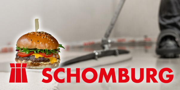 Ein Cheeseburger mit eingelegtem Pickel liegt über dem Hintergrund einer Person, die auf dem Boden ein Bauwerkzeug benutzt, mit dem roten Text SCHOMBURG und seinem Logo am unteren Rand.
